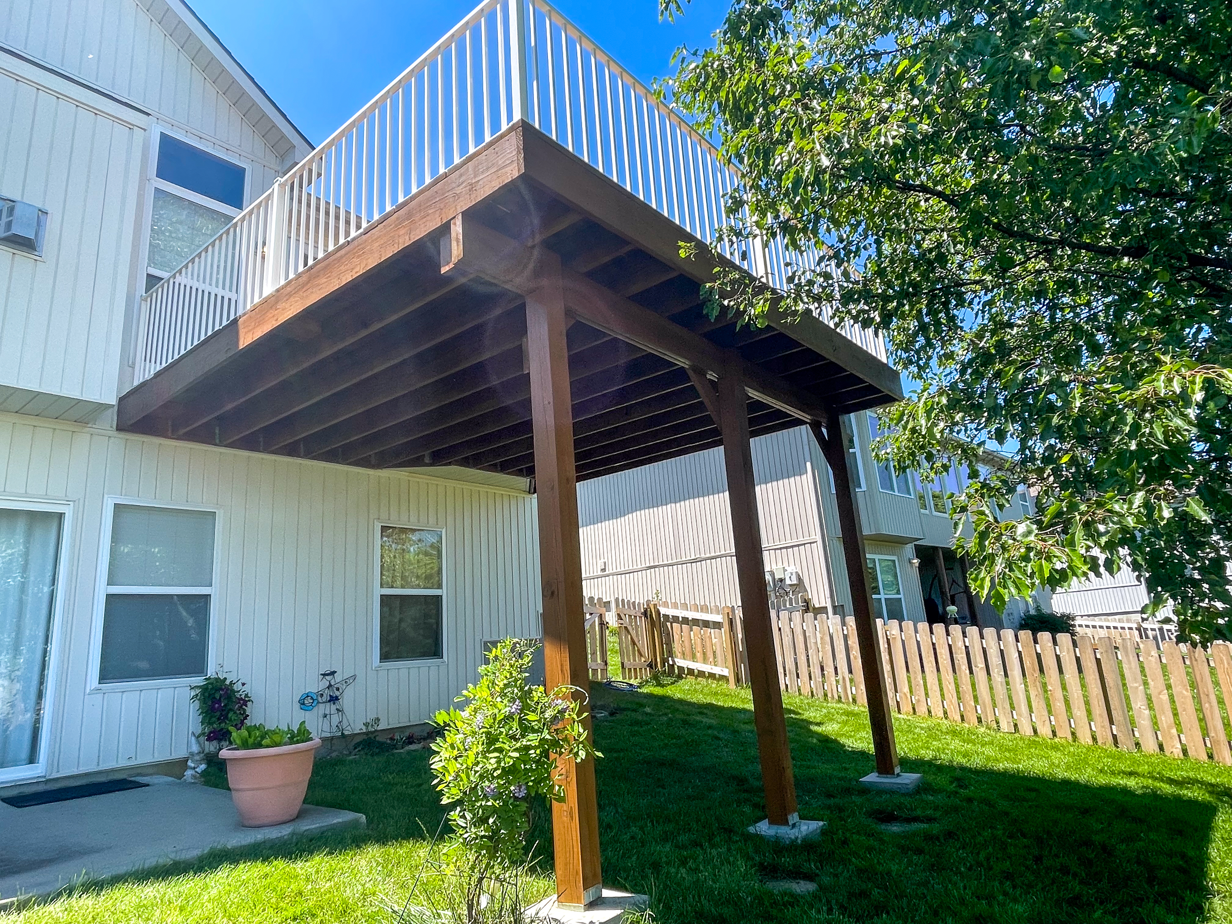Elevated wood back deck with white railings in Independence, MO by Red Letter Painting